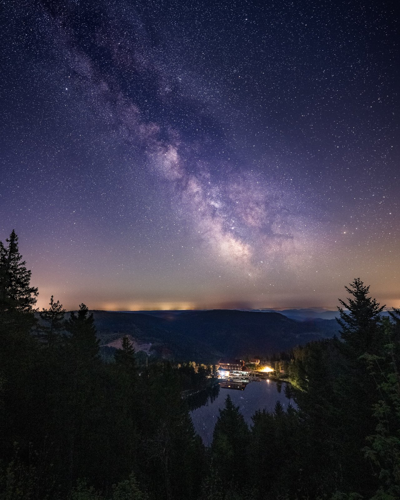 Milchstraße über einem beleuchteten Schwarzwaldsee in der Nacht