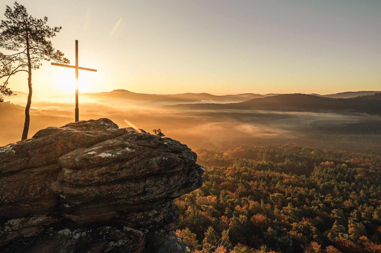 Gipfelkreuz auf Sandsteinfelsen beim Sonnenaufgang über Herbstlandschaft
