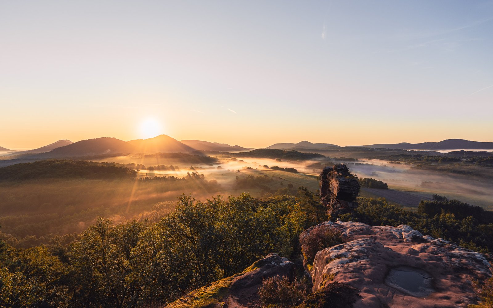 Sonnenstrahlen brechen über weites Nebeltal bei Sonnenaufgang