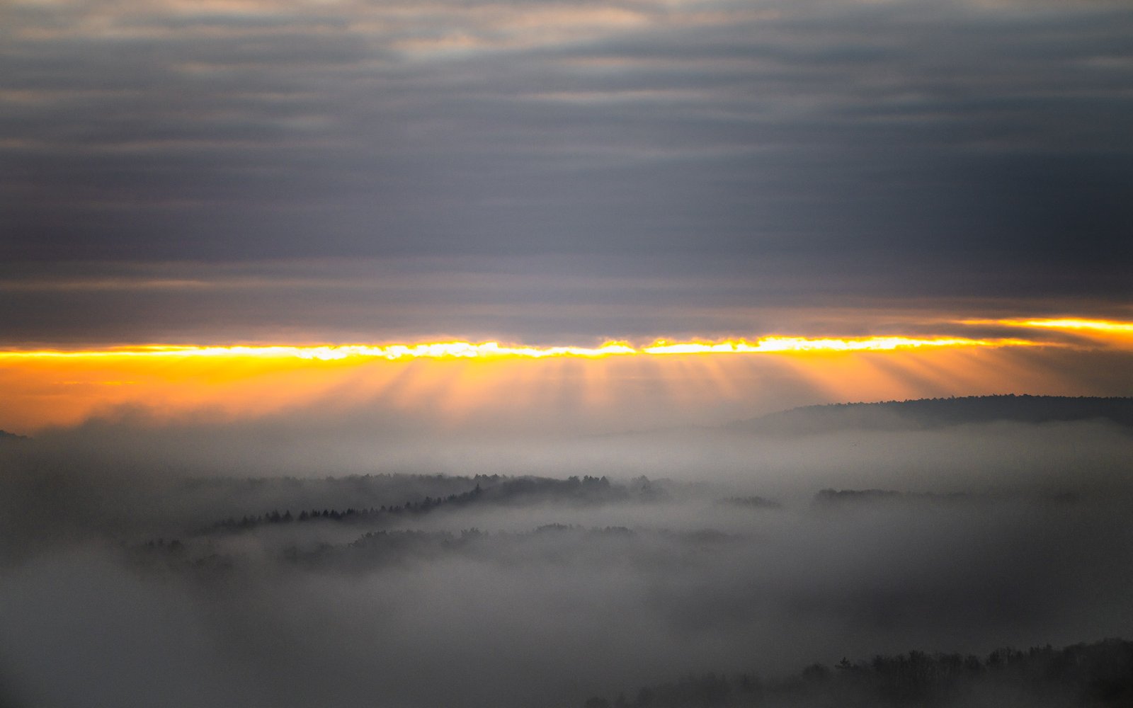 Goldene Sonnenstrahlen brechen durch Wolken ins Nebelmeer
