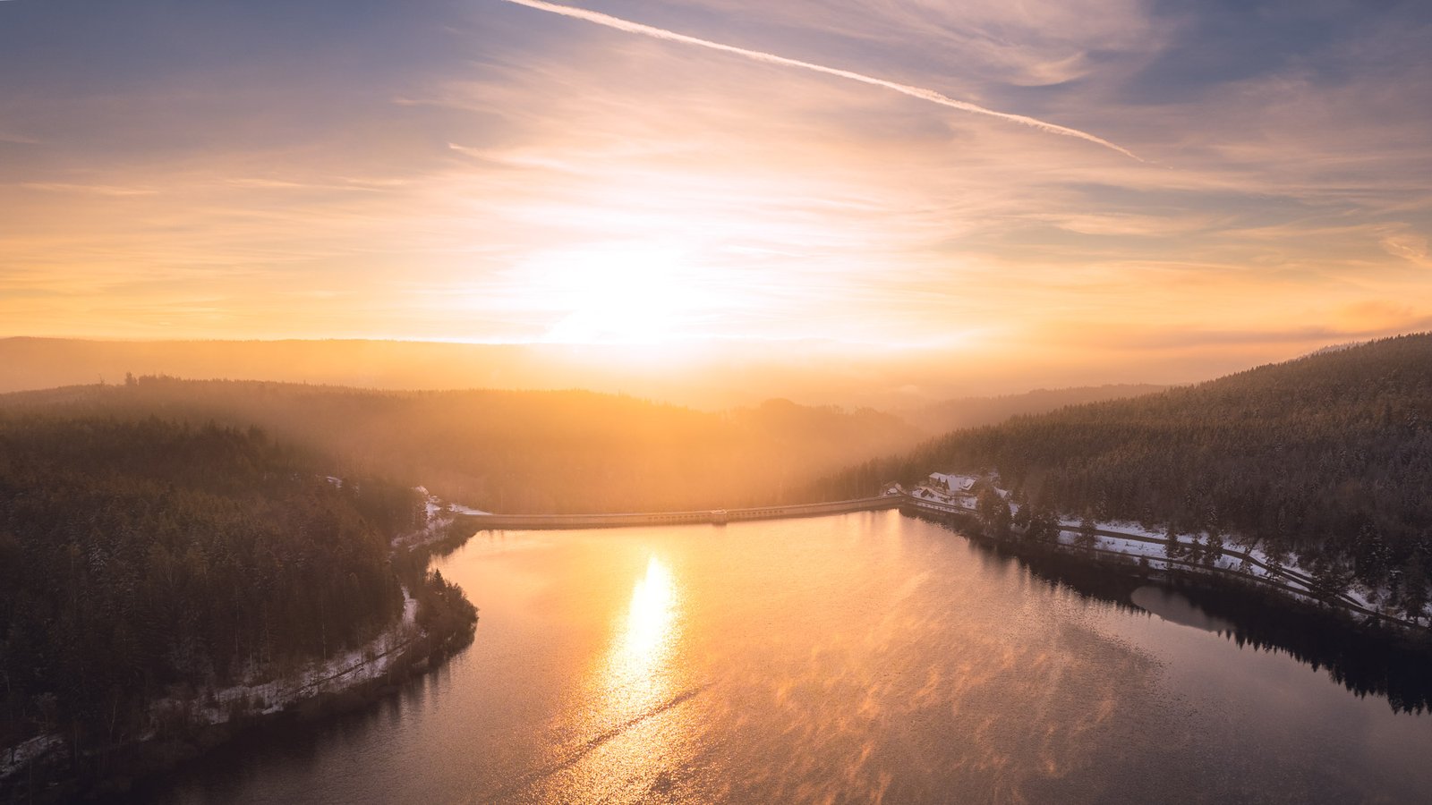 Drohnenaufnahme eines Schwarzwaldsees im Winter mit Sonnenspiegelung